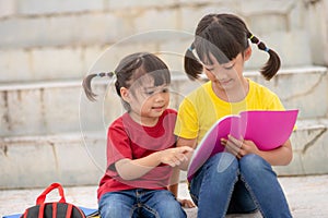 Little Girl and sister reading a book together. Adorable Asian kids enjoying studying outdoors togther. Education photo