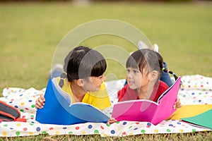 Little Girl and sister reading a book together in the park. Adorable Asian kids enjoying studying outdoors togther. Education,