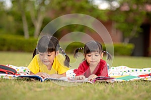 Little Girl and sister reading a book together in the park. Adorable Asian kids enjoying studying outdoors togther. Education, photo