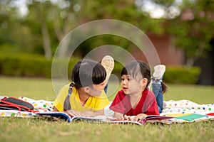 Little Girl and sister reading a book together in the park. Adorable Asian kids enjoying studying outdoors togther. Education, photo