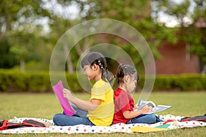 Little Girl and sister reading a book together in the park. Adorable Asian kids enjoying studying outdoors togther. Education, photo