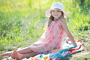 Little girl sit on green grass in summer park. Funny kids emotions. Outdoor close up portrait of a cute little child