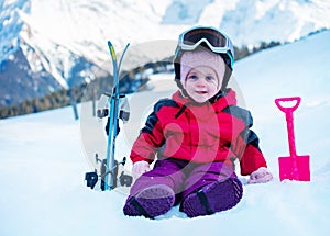 Little girl sit on snow with small mountain ski in sport outfit