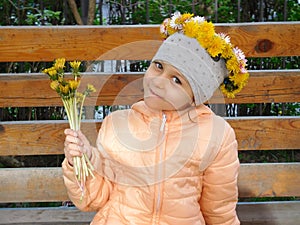Little girl sits on bench with floral wreath on her head