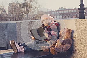 Little girl sits on a bench and reads the book to a toy bear