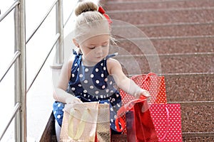 Little girl sits with colored bags on the steps in the mall