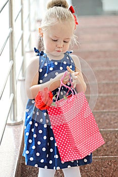 Little girl sits with colored bags on the steps in the mall