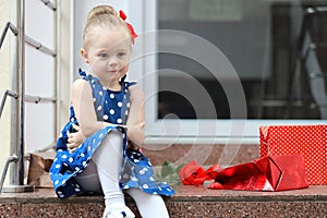 Little girl sits with colored bags on the steps in the mall