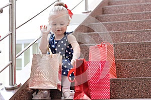 Little girl sits with colored bags on the steps in the mall