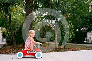 Little girl sits down by swinging her leg over the seat onto a toy car. Side view