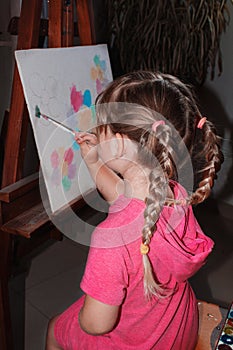 A little girl sits at the easel and draws.