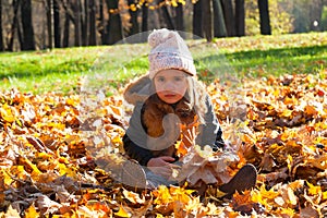 Little girl sits on fallen leaves