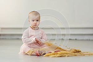 A little girl sits on the floor with an armful of wheat ears. One-year-old baby on the floor in an empty room with a