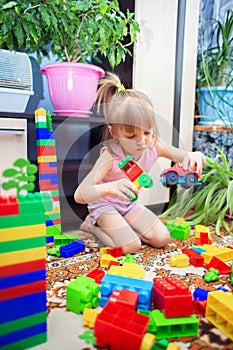 A little girl sits on the floor at home and plays a multi-colored plastic constructor. A child playing a toy train