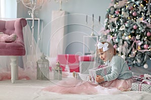 A little girl sits on the floor and unpacks Christmas boxes with gifts