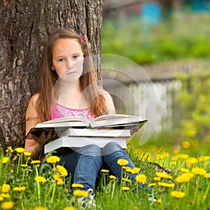 Little girl sits on a grass while reading a book