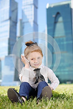 Little girl sits on grass and talks by cell phone