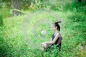 A little girl sits in the green grass with a big dandelion in her hands. Summer bright photo
