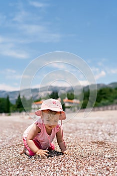 Little girl sits on her knees on the beach and digs a hole. Villa Milocer, Montenegro