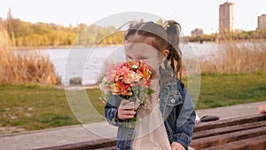 Little girl sits on a park bench with a bouquet of flowers, she sniffs flowers.
