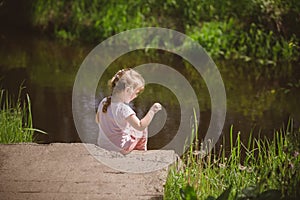 Little girl sits by the river in the forest
