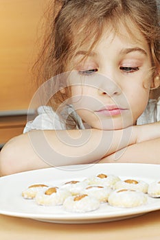 Little girl sits and sadly looks at plate with cookies