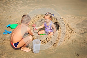 Little Girl Sits among Sand Heap Boy Squats by Play on Beach