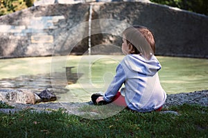 The little girl sits on the shore of the pond