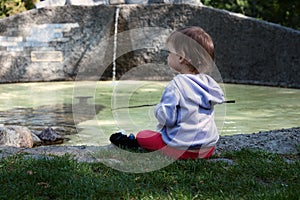 The little girl sits on the shore of the pond