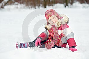 Little girl sits on snow in park