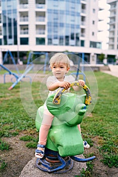 Little girl sits on a spring swing on a playground in the courtyard of an apartment building