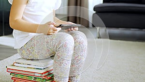 Little girl sits on stack of children's fairy-tale books and watches cartoons on her smartphone