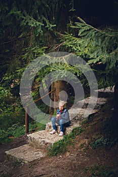 A little girl sits on a stone staircase in a mountain forest, rests