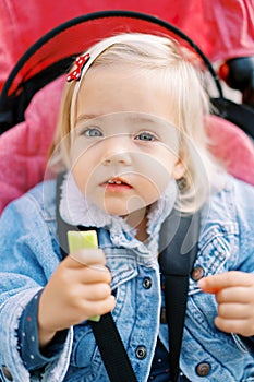 Little girl sits in a stroller strapped in with a candy in her hand