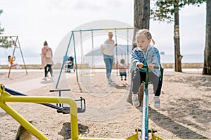 Little girl sits on a swing-balancer in the playground and looks down