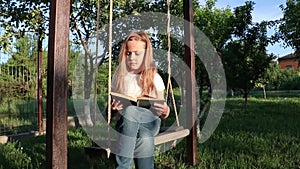 A little girl sits on a swing and writes a letter