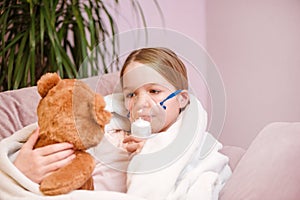 Little girl Sits with toy on sofa at home in a mask for inhalations, making inhalation with nebulizer at home inhaler