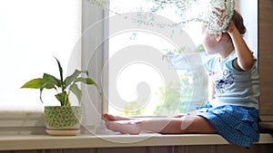 Little girl sits on a window sill and looks out the window. The concept of expectation.