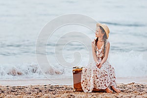 A little girl sits on a yellow suitcase on the beach