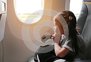 Little girl sitting in airplane and praying near the window. Adorable little girl traveling by an airplane