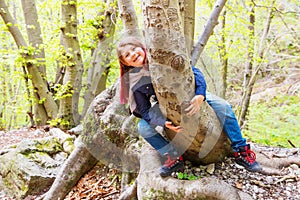 Little girl sitting astride a log in a forest