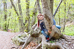 A little girl sitting astride a log in a forest