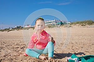 Little girl sitting on the beach looking at with angry expression face