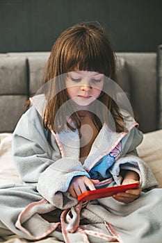 A little girl sitting on the bed, fixated on her smartphone as she interacting with digital content