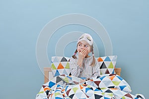 Little girl is sitting in bed in pajamas with lights on, yawning over blue