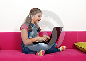 Little girl sitting on bed and playing laptop at home