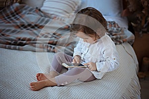 Little girl sitting on the bed with a smartphone.