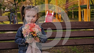 A little girl is sitting on a bench with a bouquet of flowers in a spring Park.