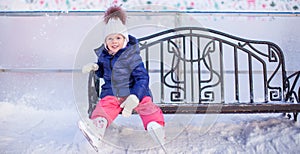 Little girl sitting on a bench in the skating rink