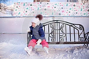 Little girl sitting on a bench in the skating rink